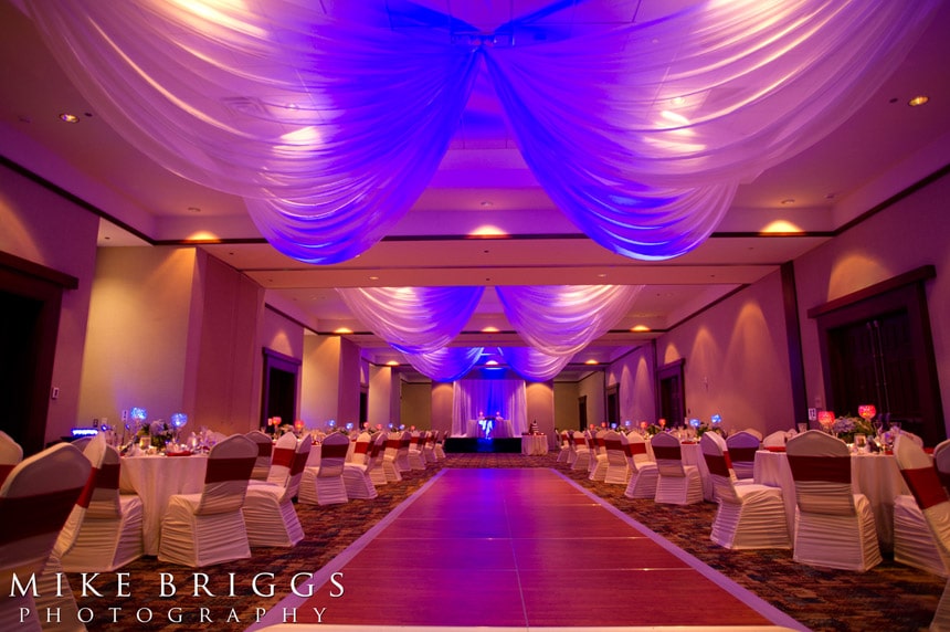 ballroom with purple lighting, white chairs, and dance floor in center